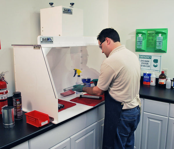 Person working in a laboratory setting with Ductless Benchtop Fume Hood, safety equipment and chemicals.