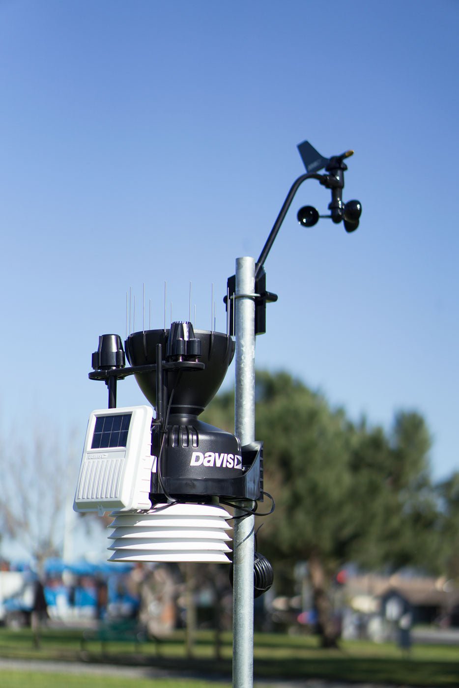 Weather station accessory by Davis Instruments, mounted on a silver pole outdoors, against a blue sky.