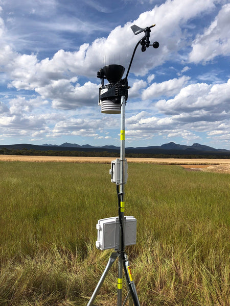 Mounting tripod by Davis Instruments on a metal pole with monitoring equipment atop, standing in a grassy field.
