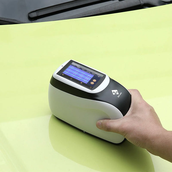 Multi-angle spectrophotometer by 3nh held over a glossy, light-green surface with a digital display screen.
