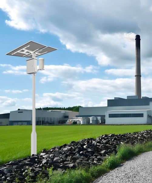 Outdoor air quality monitor by Tongdy with a solar panel, set against a green field and industrial backdrop.
