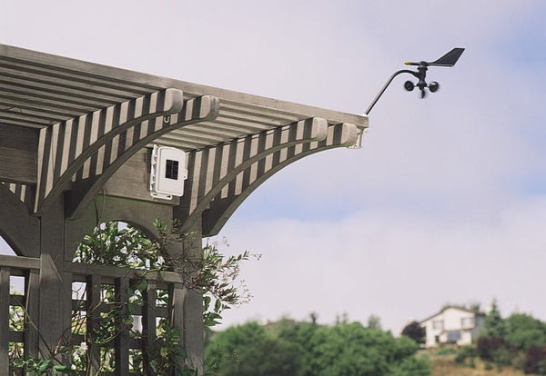 Wireless sensor transmitter by Davis Instruments mounted on a wooden pergola, with a nearby anemometer.
