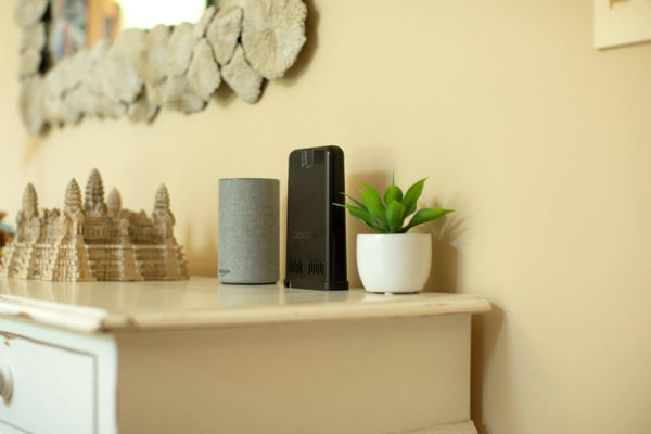 Data collection hub by Davis Instruments with ventilation slots, sitting next to a gray cylindrical speaker and small potted plant.