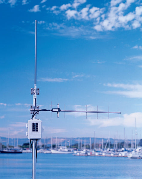 Wireless long-range repeater with solar power by Davis Instruments, with a metallic antenna and a white enclosure, against a marina backdrop.
