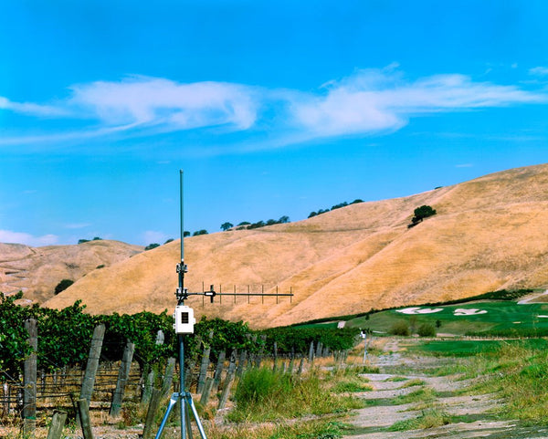 Wireless long-range repeater with solar power by Davis Instruments against a hilly landscape with vineyards and a blue sky.
