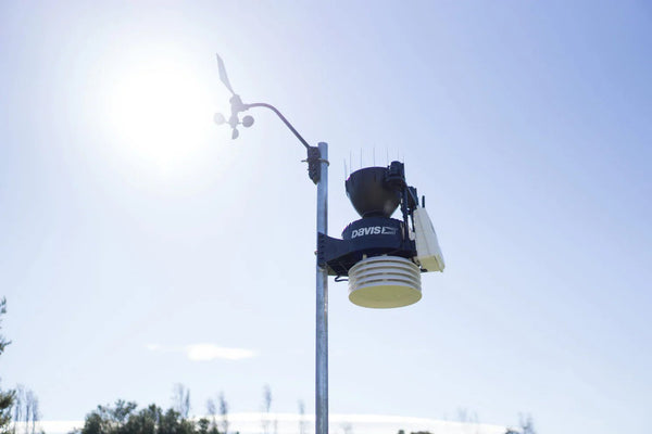 Complete weather station by Davis Instruments with a wind vane, mounted on a silver pole against a clear blue sky.
