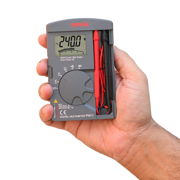 Gray pocket digital multimeter by Sanwa, held in a person's hand with visible test leads in a side compartment.
